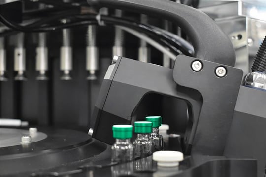 Automated laboratory machine handling vials with green caps.