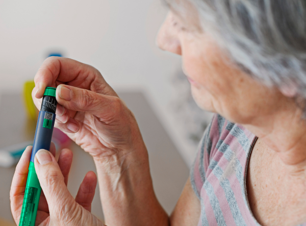 Elderly woman using an insulin pen, showcasing Syntegon's high-speed RTU solutions for precise and sterile insulin cartridge filling