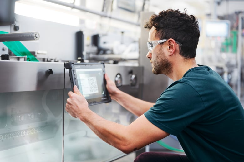 Techniker scannt mit einem Tablet ein Maschinenteil in einer modernen Produktionsanlage.