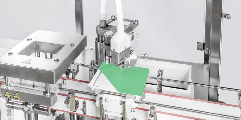 Syntegon automated machine applying a sterile film to a ready-to-use (RTU) container in a pharmaceutical processing line. High-precision robotic arm ensures sterile and efficient sealing for safe drug packaging.
